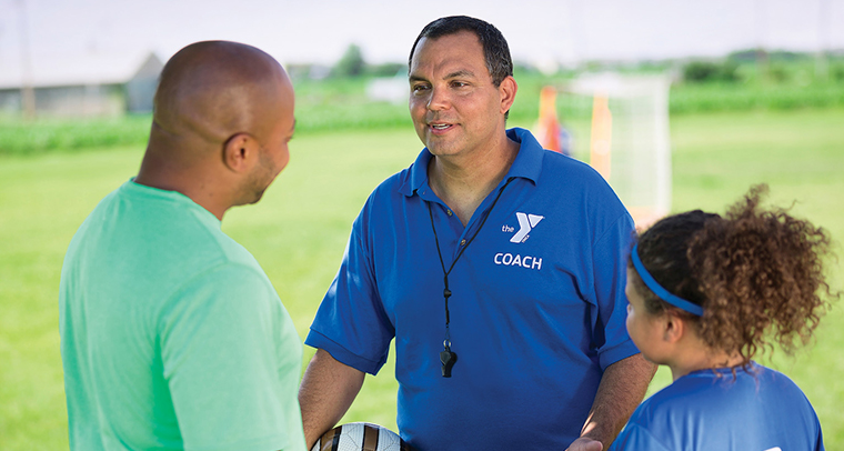 YMCA coach talking with parent and child after a soccer game