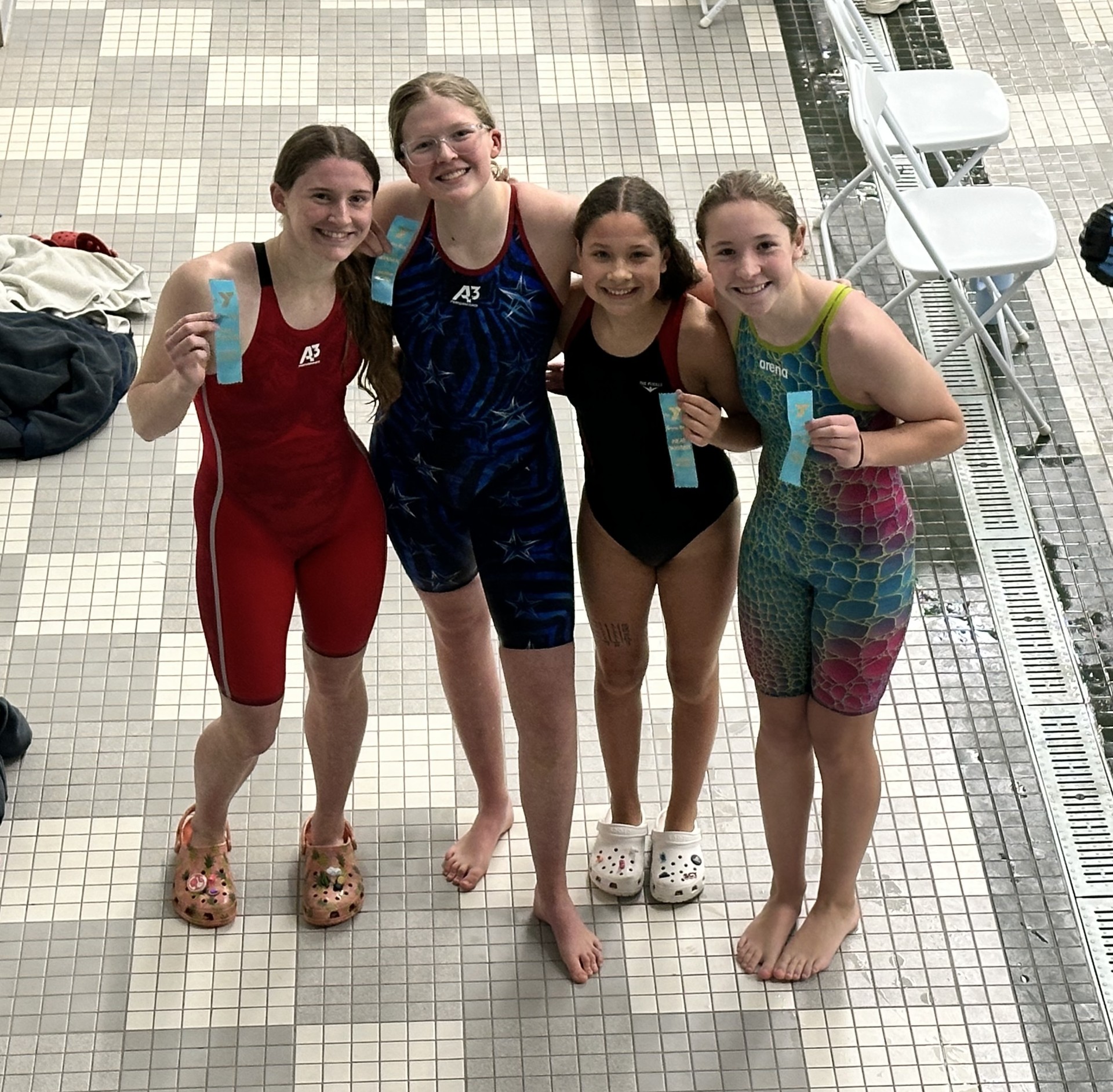 Smiling group of kids in swim suits wearing bathing caps and goggles